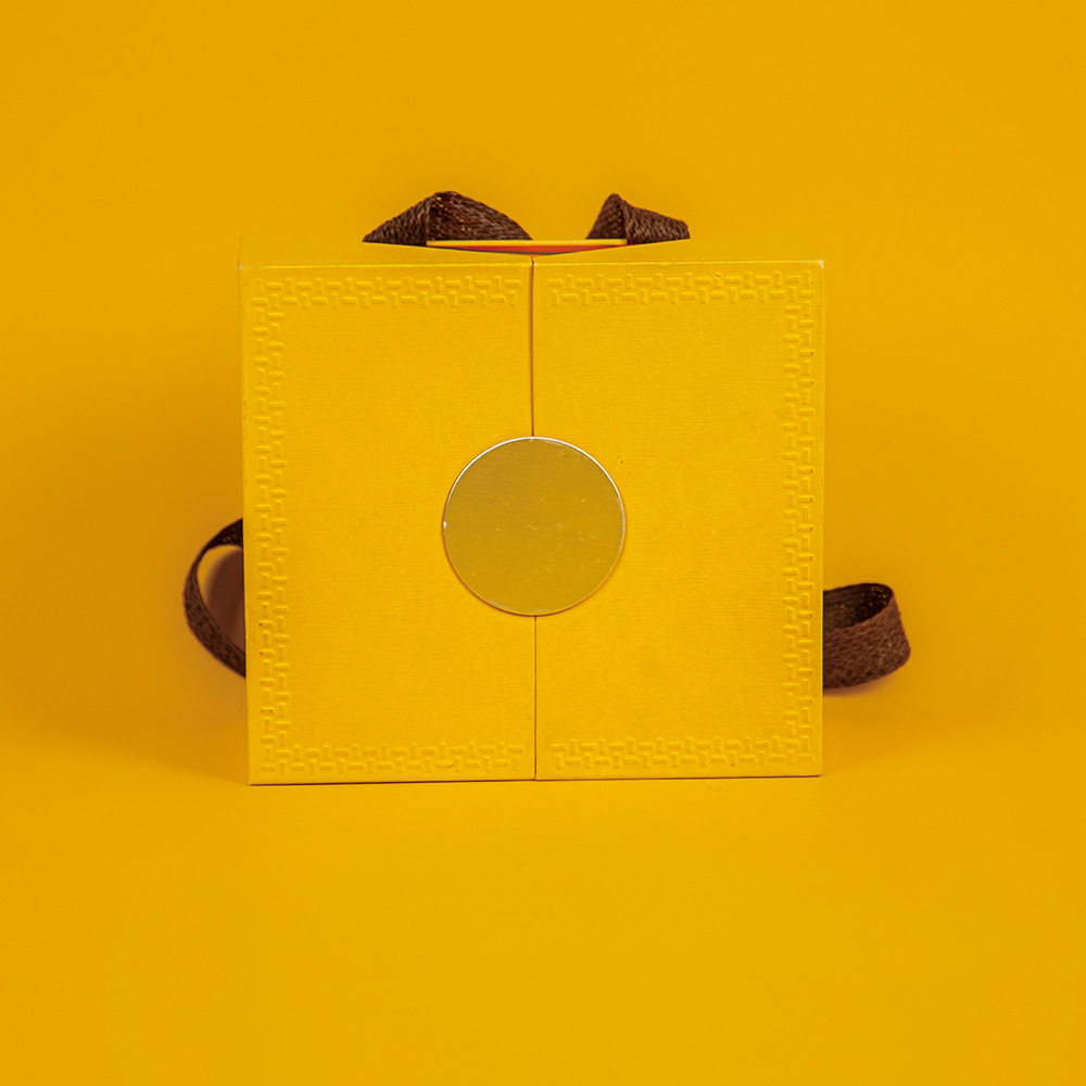 Front view of custom luxury yellow rigid gift box with ribbon handle for wholesale.